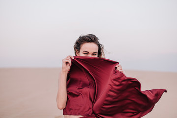 Girl with red cloth in the sunset rays in the desert
