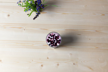 flat lay of Glass with healthy smoothie dessert prepared of basil seeds, yogurt, blueberries on wooden background and bouquet of forest flowers