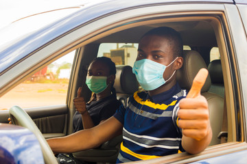 young black man and woman driving in a car with both of them wearing nose mask