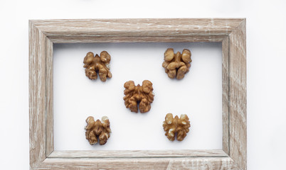 Many crushed walnuts lie on a white background in a wooden frame. Decorative photo frame. Abstraction.