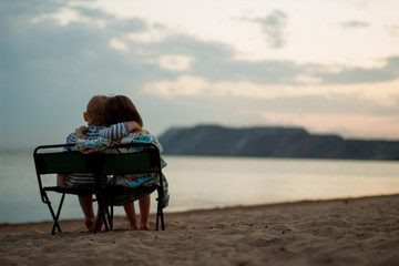 Fototapeta premium a boy and a girl sit on chairs on the beach in the evening