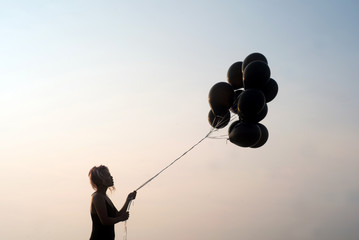 Woman in silhouette looking at black balloons about to let go set against a stark clean background...