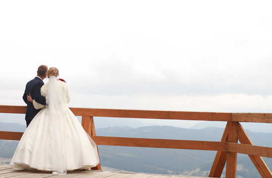 The bride and groom are standing on the edge of the board and looking up the mountain.
