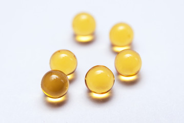 Six yellow transparent fish oil capsules on a white background