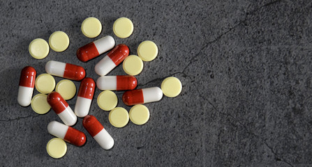 Yellow and white and red antibiotic pills from a jar on a dark concrete table