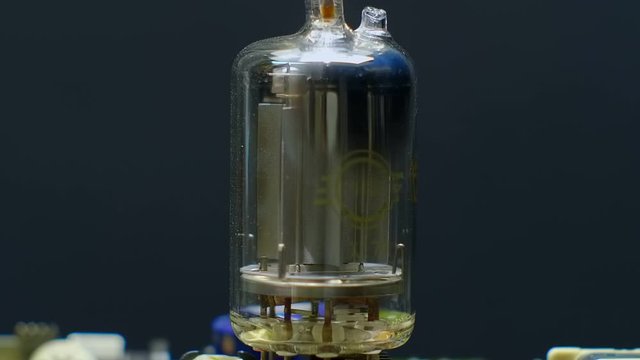 Old vacuum electronic lamp stands on a modern digital electronic board on a black background. Macro. Closeup. Shallow depth of field. Rotation
