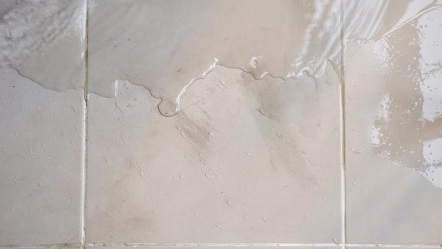 transparent water spreads across floor white tile top view