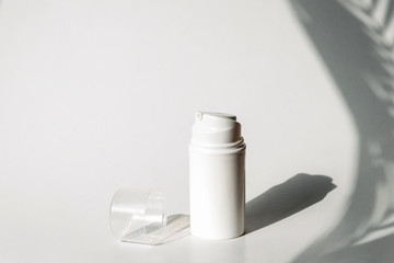 Dispenser for cosmetics products. Skincare and beauty concept. White background with shadows of tropic plants