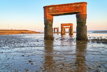 pillars of the former landing bridge in Eckwarderhörne, municipality of Butjadingen, district Wesermarsch, Germany in scenic evening sunlight during low tide