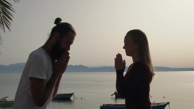 Side view of yoga teacher and student put hands in namaste and hugs at seaside