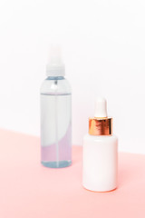 Two bottles with serum and cosmetic lotion on pink table against white wall. Unbranded blank packages. Natural skincare products concept.