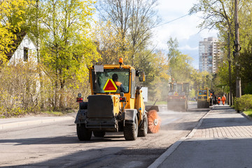 Tractor with spinning brush cleaning newly laid asphalt. Reconstruction and repair of a street road, municipal work. 
