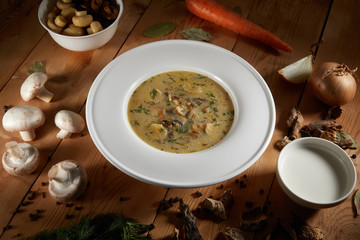 Mushroom Cream Soup with Herbs and Spices in white plate on Wooden Background. Creamy Soup Made of Champignons, Vegetables and Cream. Homemade mushroom soup food photgraphy recipe idea.