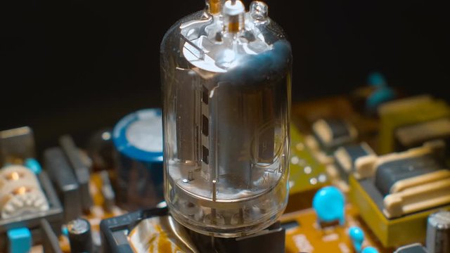 Old vacuum electronic lamp stands on a modern digital electronic board on a black background. Macro. Closeup. Shallow depth of field. Rotation