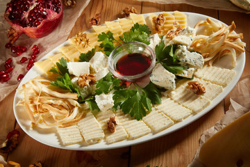 Cheese plate with different types of cheese with honey and nuts. Sliced pieces of cheese on a wooden table