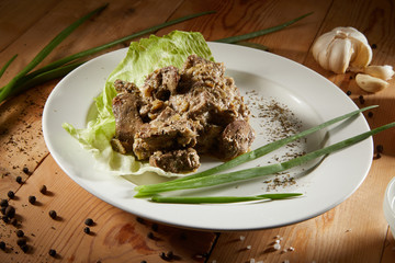 Fresh veal liver ragout in red wine sauce with onion and cram as close-up on a white plate on wooden background. Liver curry on a white plate