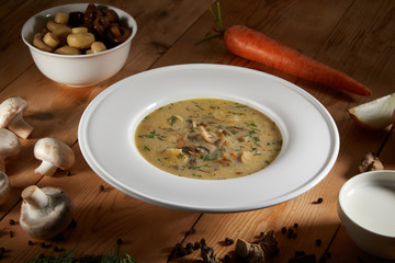 Mushroom Cream Soup with Herbs and Spices in white plate on Wooden Background. Creamy Soup Made of Champignons, Vegetables and Cream. Homemade mushroom soup food photgraphy recipe idea.