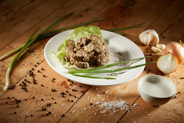 Fresh veal liver ragout in red wine sauce with onion and cram as close-up on a white plate on wooden background. Liver curry on a white plate