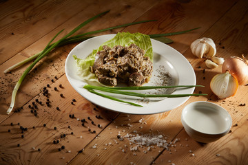 Fresh veal liver ragout in red wine sauce with onion and cram as close-up on a white plate on wooden background. Liver curry on a white plate