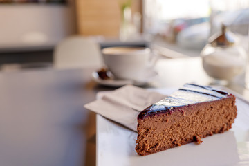 Selected focus view at simply chocolate cheese cake on white plate beside with a cup of coffee, on table beside window of bright cafe.