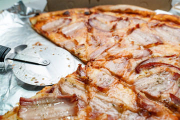 Close up on bacon and cheese pizza with two slices one quarter taken with roller cutter in empty...