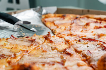 Close up on bacon and cheese pizza with two slices one quarter taken with roller cutter in empty...