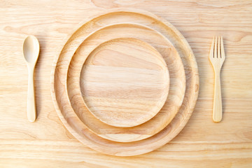 The natural rubber wood round plate, lacquered, is stacked on top of a wood cutting board, with a spoon and fork placed on it.