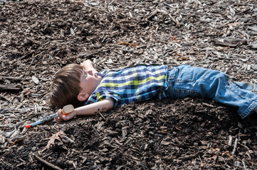 Young boy pretending to be dead while playing cowboys and holding a gun.
