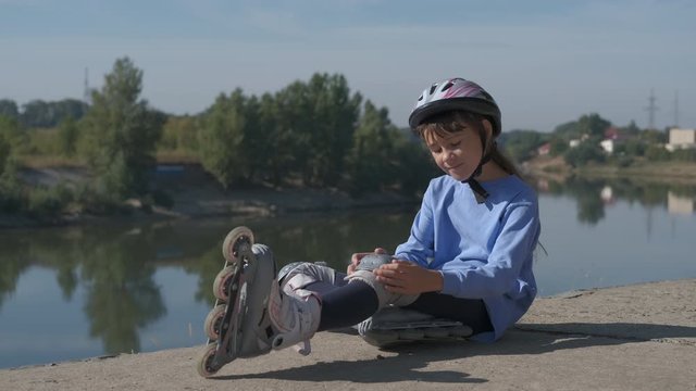 Child with roller skates. A cute teenage girl in roller skates sits on the bank of the river.