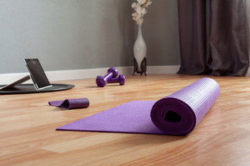 sports equipment and a tablet computer are laid out on the floor in a room. Home workouts at home using a mat, dumbbell, stretch marks. Home online fitness