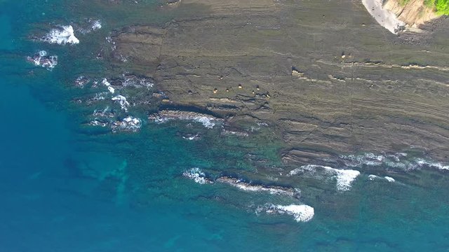 Overhead Rollback Reveal Flying Aerial View of Jicaron Island (Coiba Park) Water Edge with Slate Rock Cliff Shore and Dense Jungle Trees with Distant Islands