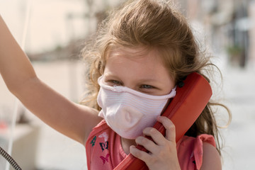 cute little girl is talking on a public phone during the covid-19 epidemy in Venice