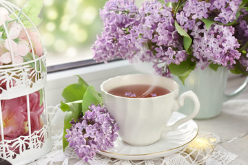 Obraz na płótnie Canvas cup of tea and bunch of lilac blossom on window sill