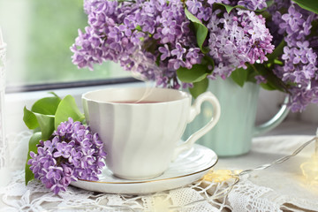 cup of tea and bunch of lilac blossom on window sill