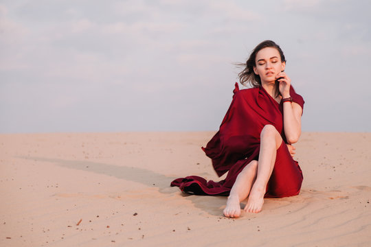 The girl in the red dress sits in the wind in the desert