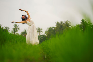 Naklejka premium mind and body connection with nature - middle aged attractive and happy Asian Chinese woman in Summer dress enjoying idyllic tropical destination dancing free