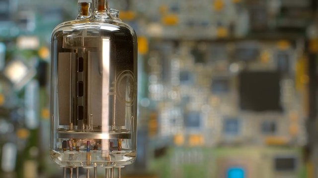 Old vacuum electronic lamp stands on the background of a modern digital electronic board. Macro. Closeup. Shallow depth of field. Rotation