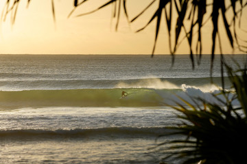 Fototapeta na wymiar Silhouette of a surfer riding a wave during a colourful sunrise.