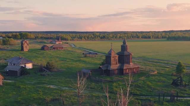 Abandoned wooden buildings: a church, a windmill, a farmhouse and a cottage on the abandoned deserted outskirts of the village at summer sunset. Aerial view