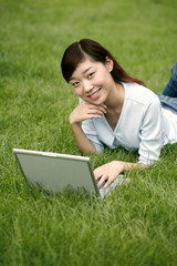 Female student lying on field using laptop