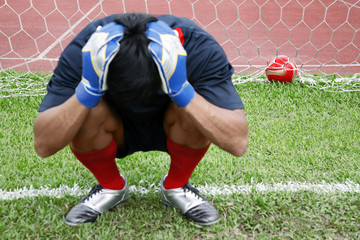 Man kneeling in goal holding head in hands