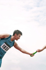 Two men's hands passing the baton in a relay race