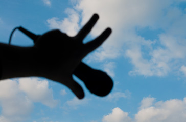 Fototapeta na wymiar silhouette of a hand with a microphone on a background of blue summer sky with clouds