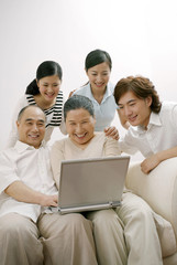 Senior man and woman using laptop with family members watching
