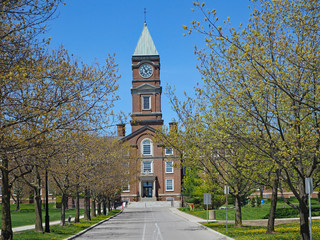 New England style brick school or college building with clock tower behind avenue of trees