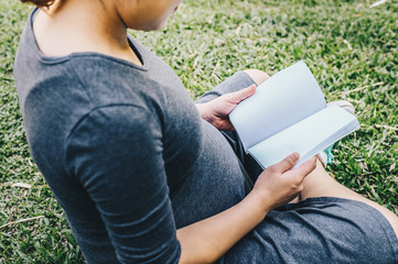 Cropped shot view of young pregnant woman sitting in the garden, open and reading a book (a book with blank space). Conceptual of pregnant woman lifestyle. © boyloso