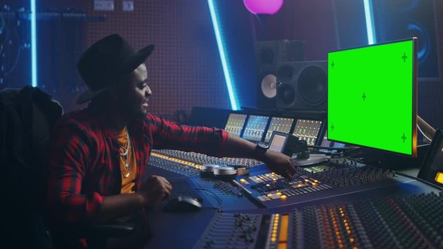 Portrait of Stylish Audio Engineer / Producer Working in Music Record Studio, Uses Green Screen Computer, Mixer Board, Control Desk to Create New Song. Creative Black Artist Dances while Sitting