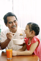 Senior man feeding girl cereal