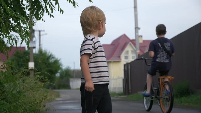 Little Boy Watching on Bicyclist while Walking and Playing on Rural Road. Evening Suburbs. 2x Slow motion - Half Speed 60 FPS