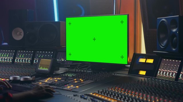 Portrait of Stylish Audio Engineer Working in Music Record Studio, Uses Green Screen Computer, Mixer Board, Control Desk to Create New Song. Creative Black Artist Dances while Sitting. Over Shoulder
